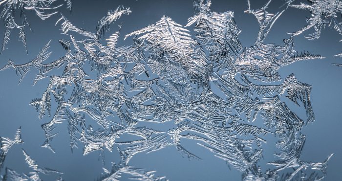 A closeup shot of a snowflake on a glass from frost, with detailed pattern